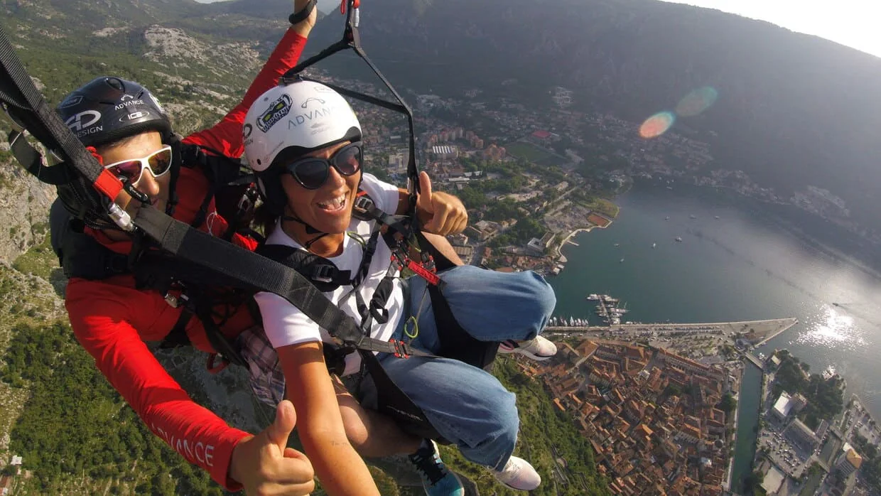 Passenger and pilot flying tandem above the Bay of Kotor with the town below.